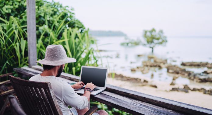 A man works on his computer in front of the sea